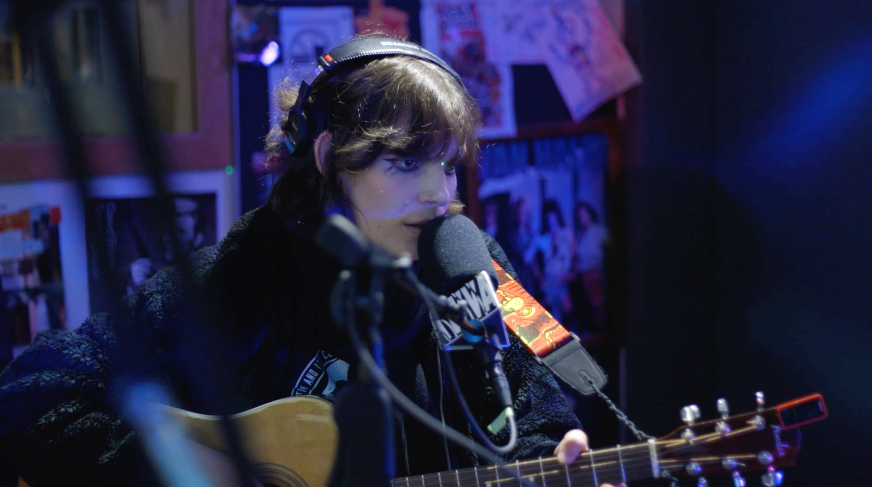 Young trans woman wearing dark makeup sitting and holding acoustic guitar