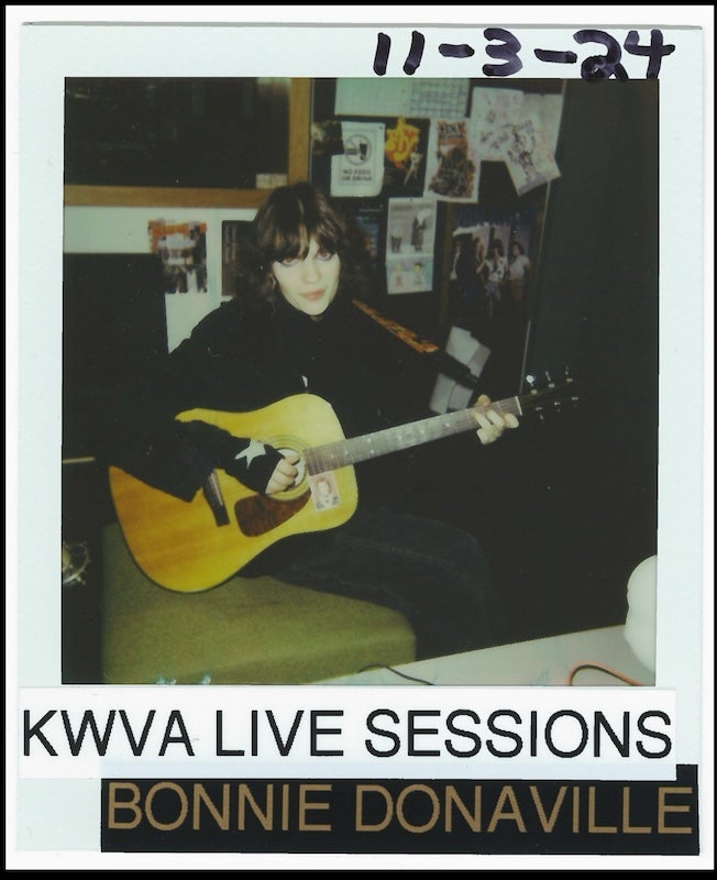 Young trans woman wearing dark makeup sitting and holding acoustic guitar