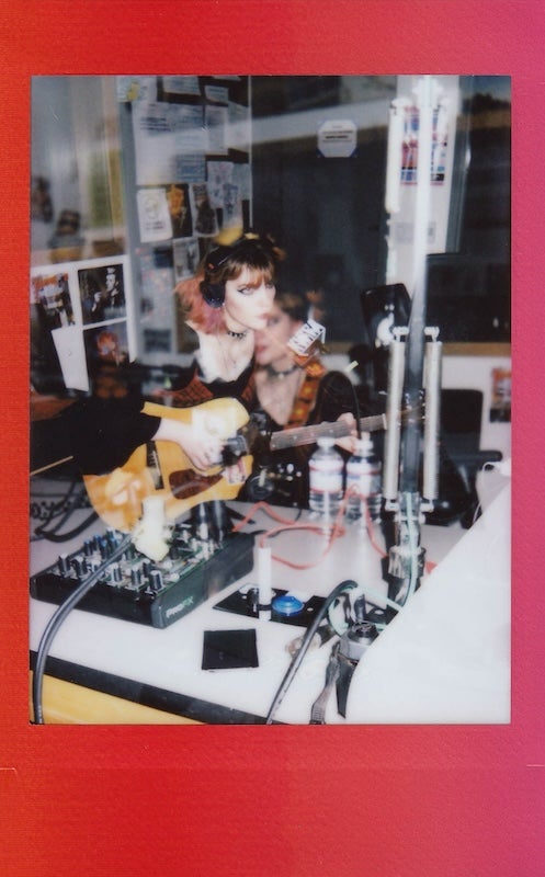 Small polaroid photo with red frame featuring a double-exposure image of artist bonnie donaville playing guitar singing and wearing headphonrs in the kwva radio studio