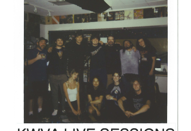 Polaroid framed picture of 11 people, 8 men and 3 women posing for a picture. Seven people are standing behind 3 sitting people. Text above read October 27th 2024, text below read KWVA Live Sessions, Blotter Boys.