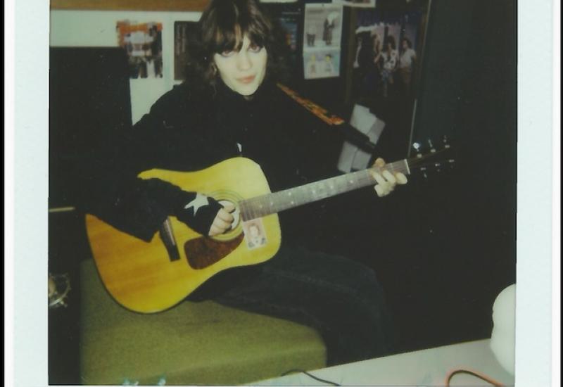 Young trans woman wearing dark makeup sitting and holding acoustic guitar