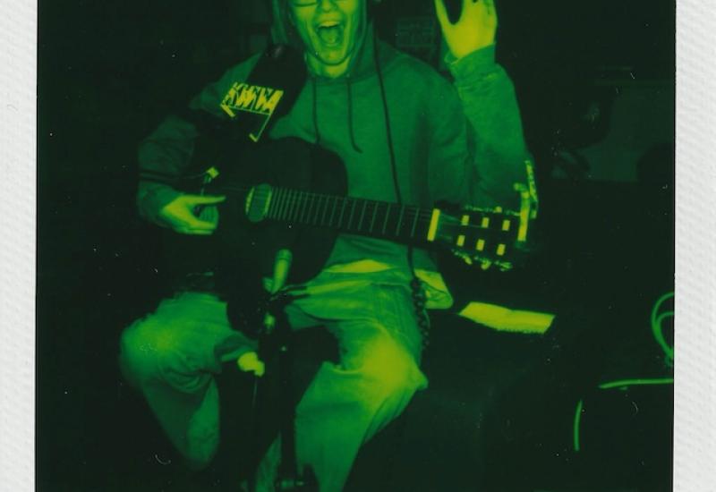 Polaroid picture with dark green filter, Trimmo, early 20's white male with glasses holding guitar. Text reads january 26th 2025, kwva live sessions, trimmo.