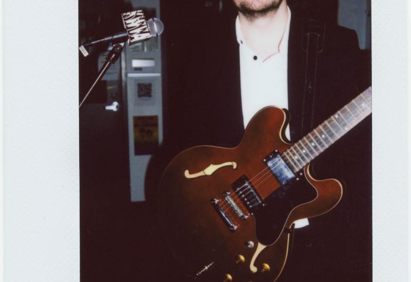 Polaroid picture of the artist known as Candy Cigarettes (white man, tall, short beard) posing in the KWVA studios